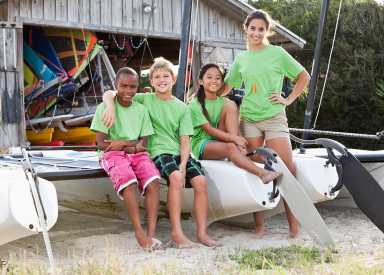 Teenage camp counselor with children sitting on catamaran at water sports equipment rental shack.