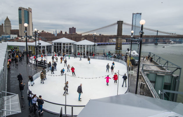 skaters on a rooftop ice rink with the brooklyn bridge in the background