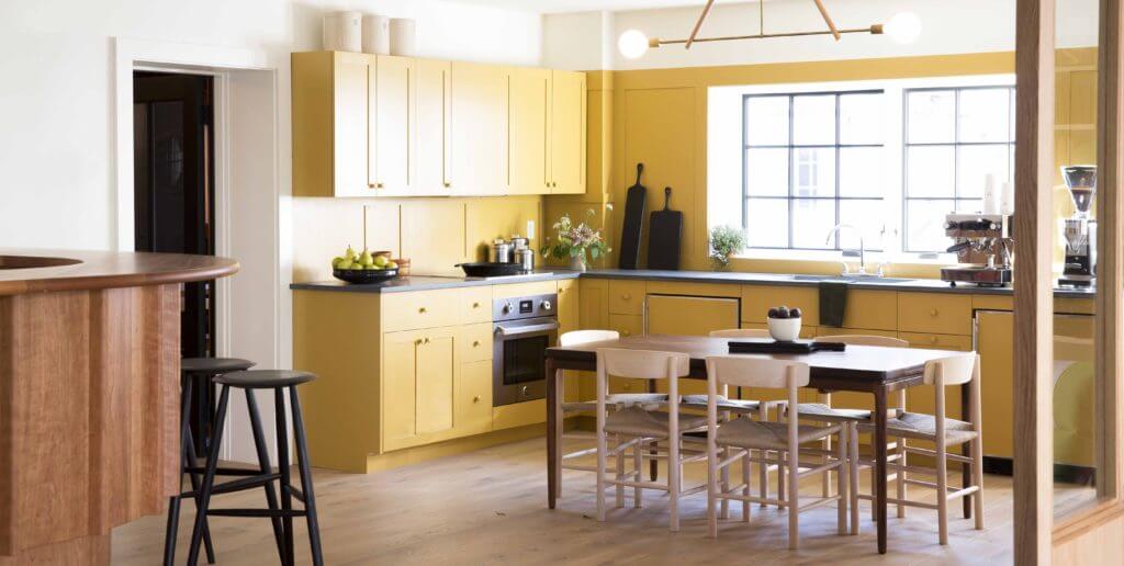 Bright kitchen with yellow cabinets, black countertops, bar area, large window, and dining table with six chairs in natural light.