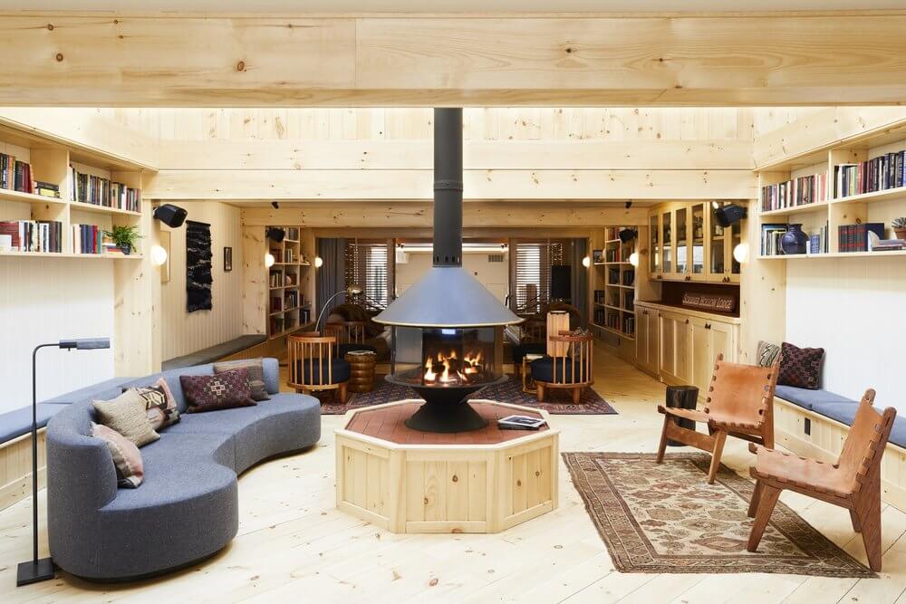 A cozy library features light wood walls, lots of bookshelves, a modern fireplace, curved sofa, and lounge chairs, creating a warm atmosphere.