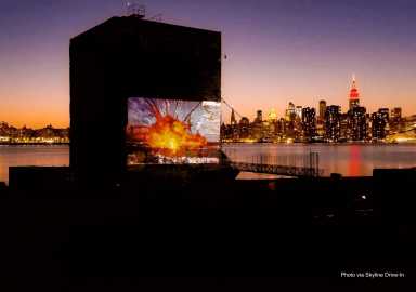 A nighttime cityscape with a movie projected on a dark riverside structure, Empire State Building lit up in the background.