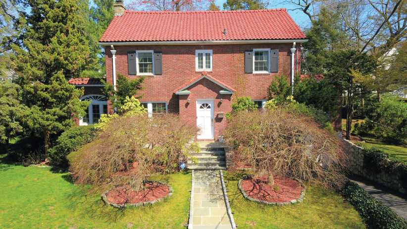 Aerial view of a modern two-story house in Pelham Manor, with a separate garage connected by breezeway, lots of green trees around.