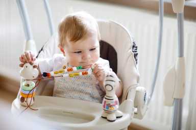 Baby sitting in a high chair, playing with colorful beads and a zebra toy, focused and curious.