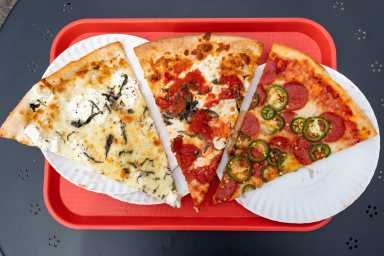Three New York City style pizza slices on a red tray, set on a table, viewed from above with bright, appetizing colors.