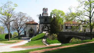 Historic Vanderbilt Planetarium features an arched stone building, leafy trees, and pathways, with a clear sky overhead and bridge in view.
