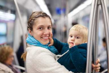 a person in white coat and teal scarf holds a child on public transit.