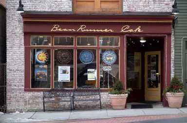 street view of a cafe with maron trim,large front windows displaying colorful signs, and a potted plant near the entrance.