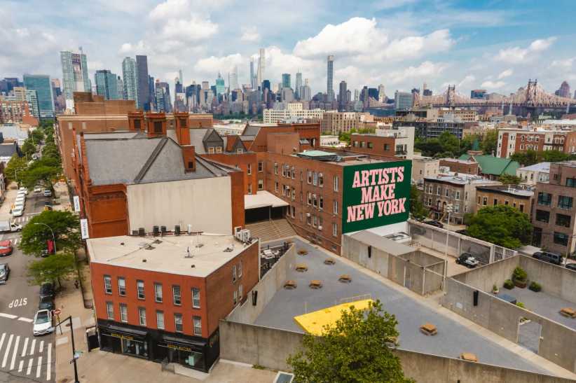 Aerial view of Long Island City, Queens with cityscape and MoMA PS1; green mural reads "ARTISTS MAKE NEW YORK" on brick building.