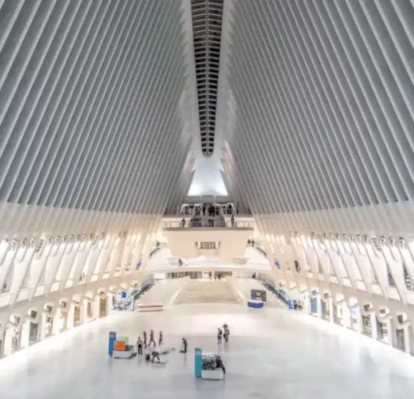 A spacious, modern hall with white floors and dramatic ribbed arches, filled with natural light and scattered people below.