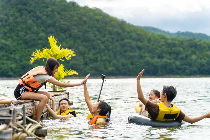 ChatGPT said:Group of friends wearing life jackets enjoying a lake swim, giving high-fives near a wooden raft with lush green hills behind.