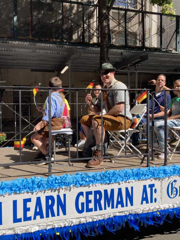 People in traditional German outfits waving flags on a parade float promoting German language learning.