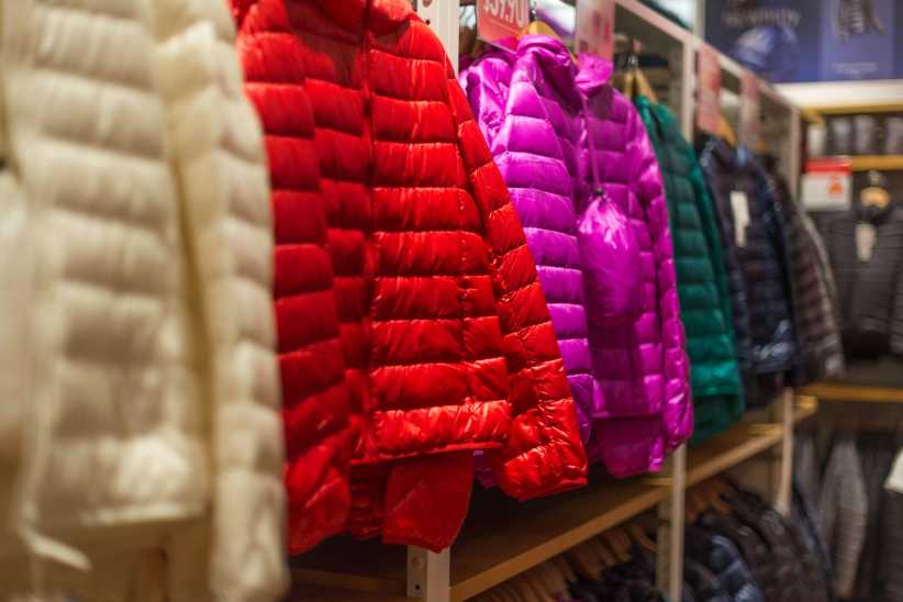 The image displays a row of colorful puffer jackets on display in a clothing store, featuring shades like red, purple, green, and white.