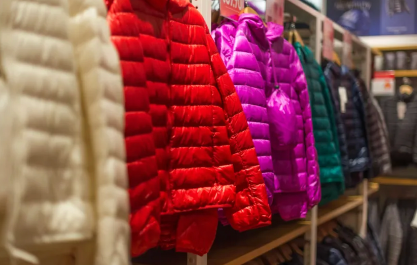 The image displays a row of colorful puffer jackets on display in a clothing store, featuring shades like red, purple, green, and white.