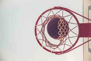 Basketball captured from below as it drops through a red hoop.